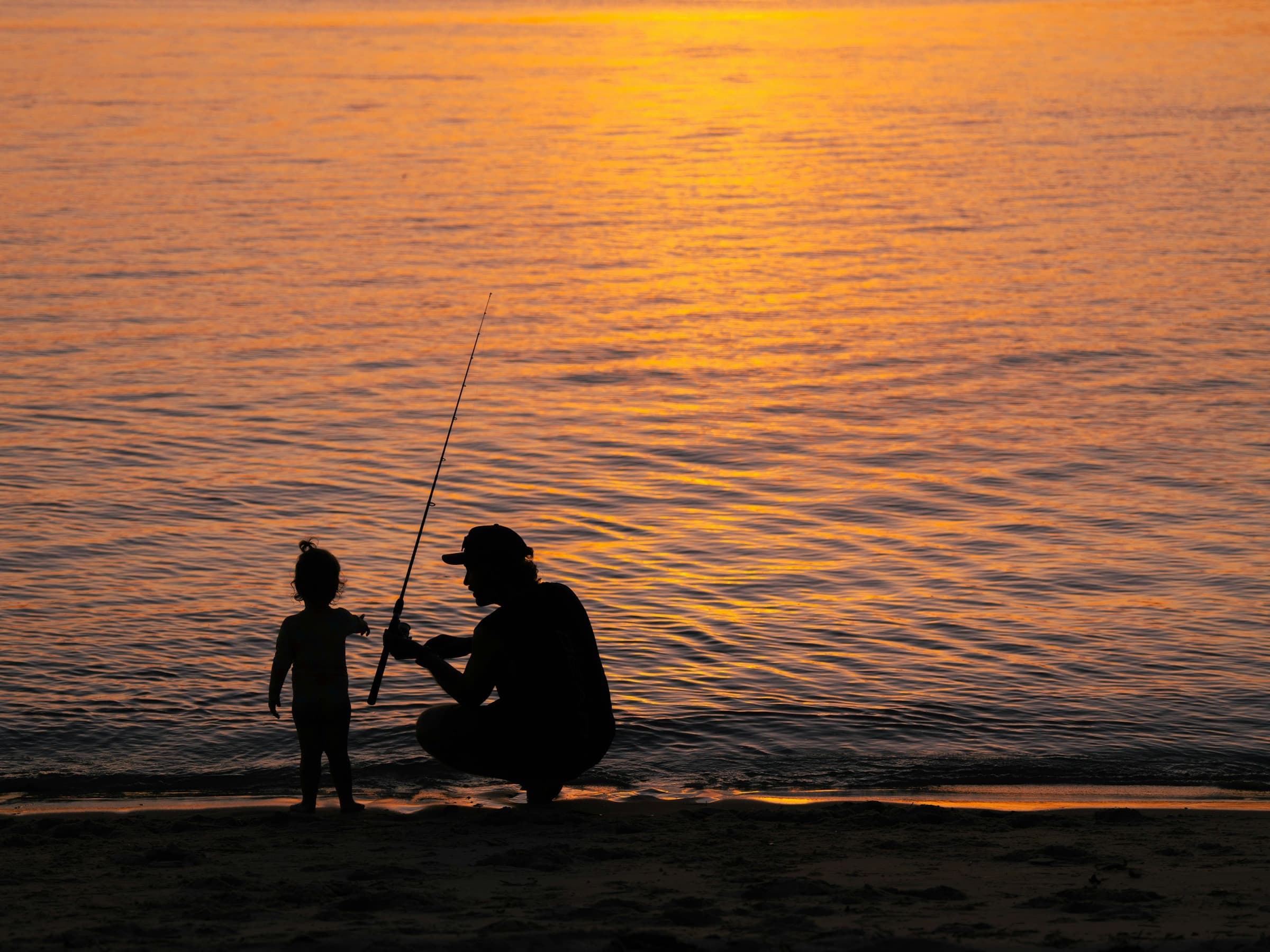 A father teaching his child to fish at sunset